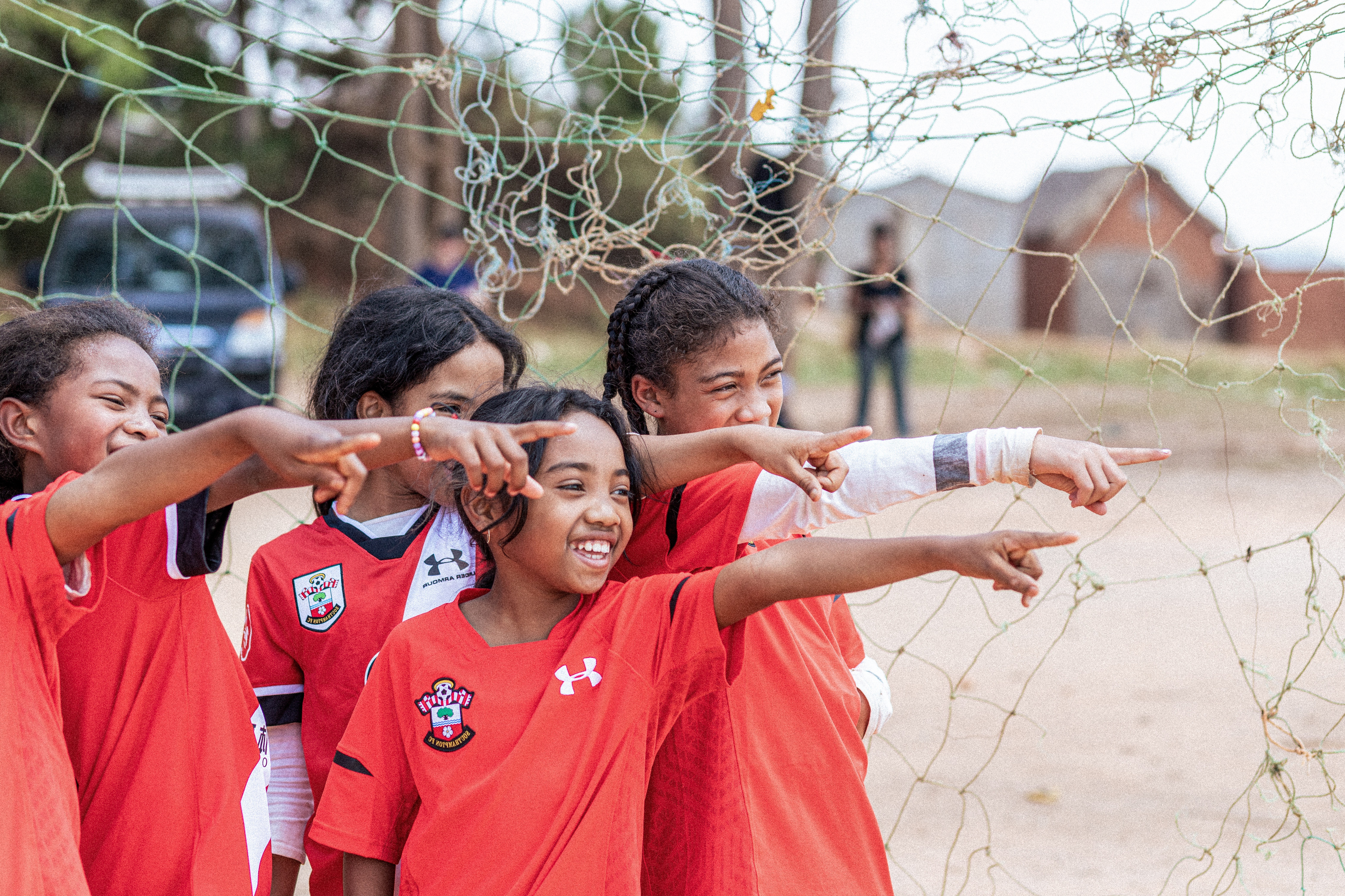 Five girls in red sports clothes, smiling and pointing to the right.